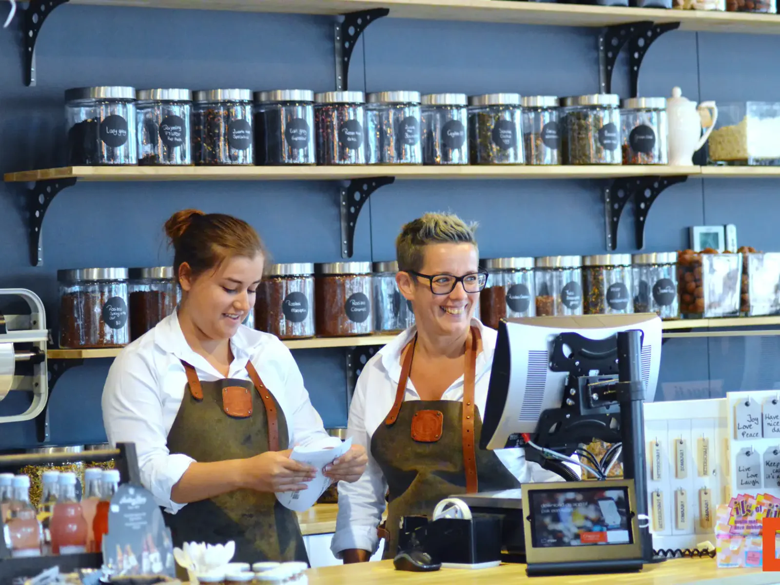 Twee winkelmedewerksters achter de toonbank met kassasysteem in een winkel vol glazen voorraadpotten
